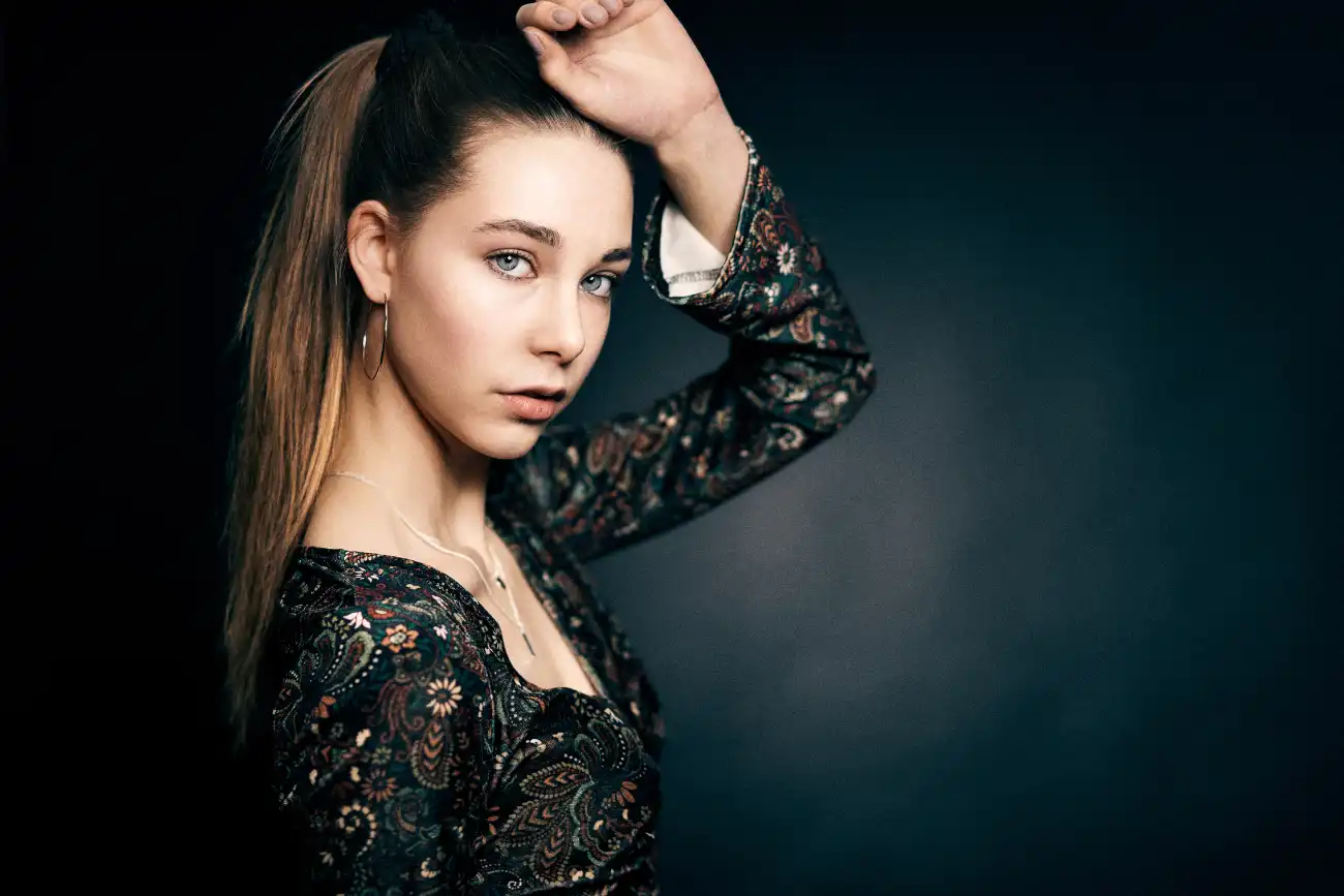 Portrait einer jungen Frau vor dunklem Hintergrund mit seitlich angehobenem Arm.